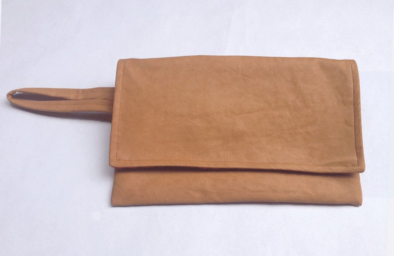 Puede incluir: Un clutch de ante marr&oacute;n con un asa de correa &uacute;nica.