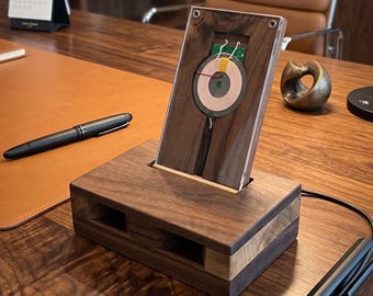 May include: A rectangular dark wood wireless charging stand featuring a visible circular copper induction coil mounted on a vertical panel. The base is constructed from solid walnut with a horizontal light wood accent strip and a black power cable.