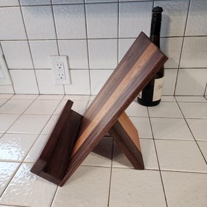 May include: A wooden cookbook stand with a walnut and maple finish. The stand is angled to display a cookbook.