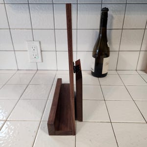 May include: A dark brown wooden stand with a shelf for displaying items. The stand is made of solid wood and has a simple, elegant design.