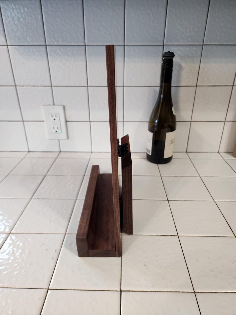 May include: A dark brown wooden stand with a shelf for displaying items. The stand is made of solid wood and has a simple, elegant design.