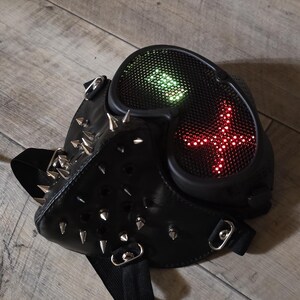 Pode incluir: M&aacute;scara de couro preta com pontas prateadas e luzes LED. A m&aacute;scara tem um design futurista com uma exibi&ccedil;&atilde;o de luz em forma de cruz em luzes vermelhas e verdes. A m&aacute;scara &eacute; projetada para cosplay ou fantasia.