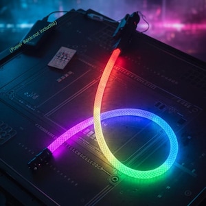 Op de afbeelding: Een veelkleurige LED-lichtkabel, met een regenboogverloop, opgerold op een donker printplaat. De kabel loopt over van rood naar paars, blauw, groen en geel. De achtergrond is een vage mix van blauw en roze.