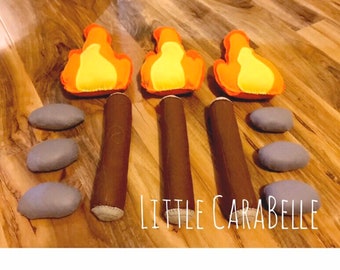 May include: Three felt campfire sets with orange flames, brown logs, and gray rocks. The sets are arranged in a row on a wooden surface. The text "LITTLE CARABELLE" is visible below the sets.