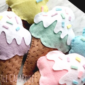 May include: Five felt ice cream cones with different colored ice cream and sprinkles. The cones are brown and the ice cream is purple, green, blue, pink, and yellow.