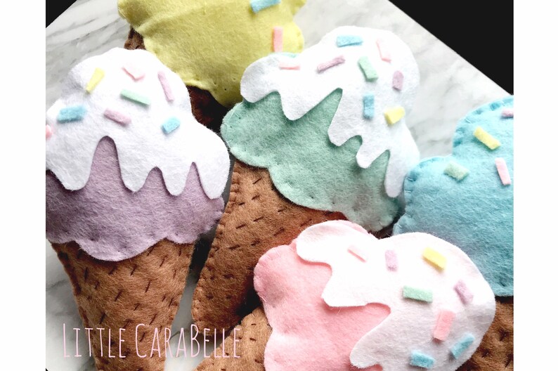 May include: Five felt ice cream cones with different colored ice cream and sprinkles. The cones are brown and the ice cream is purple, green, blue, pink, and yellow.