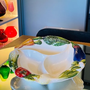 Könnte beinhalten: Eine weiße Keramik-Servierplatte mit drei Abschnitten, verziert mit bemalten Gemüse. Die Platte zeigt eine Karotte, eine Zwiebel, eine Tomate, eine Artischocke und eine Aubergine.