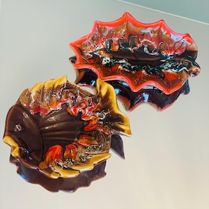 Könnte beinhalten: Zwei Keramik-Servierplatten in Form eines Fisches und eines Blattes. Die Platten sind mit brauner, orangefarbener und roter Glasur verziert.