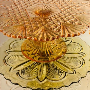 Könnte beinhalten: Ein dreistöckiger Kuchenständer aus Glas. Die oberste Etage ist rosa und hat ein Diamantenmuster. Die mittlere Etage ist gelb und hat ein Blumenmuster. Die unterste Etage ist klar und hat einen gewellten Rand.