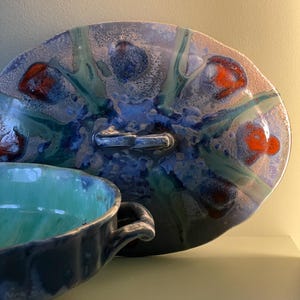 Peut inclure: Un plat de service en céramique bleu et vert avec une poignée et un bol assorti. Le plat a un glaçage marbré avec des accents rouges.