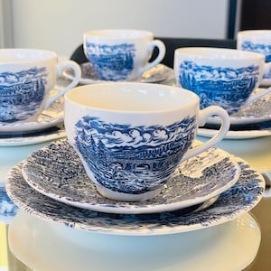 Puede incluir: Un juego de tazas y platillos de té azul y blanco con un diseño escénico. Las tazas y platillos presentan un paisaje azul y blanco con un puente y árboles.