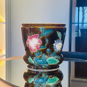 May include: A brown ceramic planter with a floral design. The planter features pink, blue, green, and white flowers and leaves.