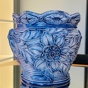 Pode incluir: Um vaso de cerâmica azul e branco com um design floral em relevo. O vaso tem uma borda festonada e uma base larga.