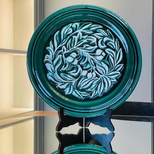 Puede incluir: Un plato de cerámica verde con un diseño floral blanco. El plato está sobre un soporte negro.