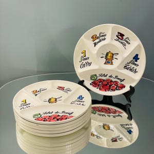 May include: A stack of off-white, divided serving plates with black trim. Each plate has five sections labeled with sauce names and numbers. The center features a gold and black illustration. The bottom of the plates display a red floral design.