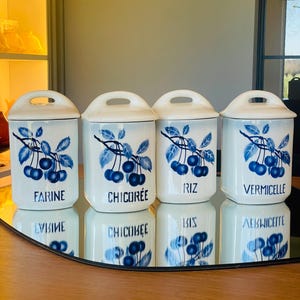Puede incluir: Cuatro botes de cerámica blanca con diseños florales azules y blancos y letras negras. Los botes están etiquetados con "Farine", "Chicoree", "Riz" y "Vermicelle".