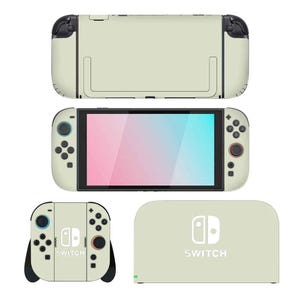May include: A light beige Nintendo Switch console skin set. The set includes the console, two Joy-Con controllers, and a dock. The controllers have black accents and colored buttons. The dock has the word "SWITCH" printed on it.