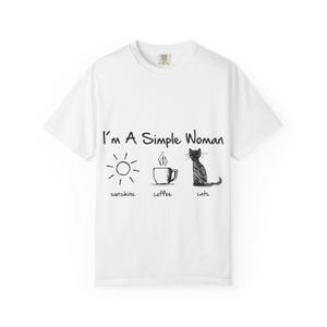 Könnte beinhalten: Weißes T-Shirt mit dem Text "I'm A Simple Woman" und Illustrationen von Sonne, Kaffeetasse und Katze. Die Wörter "sunshine", "coffee" und "cats" stehen darunter. Das Shirt ist aus weichem Material.