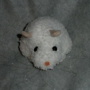 Op de afbeelding: Witte pluche speelgoed hamster met zwarte ogen en een roze neus. De hamster heeft lange witte snorharen en kleine, beige oren.