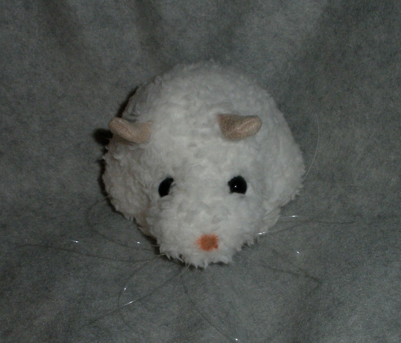 Op de afbeelding: Witte pluche speelgoed hamster met zwarte ogen en een roze neus. De hamster heeft lange witte snorharen en kleine, beige oren.