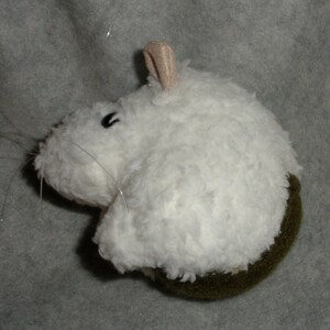 Op de afbeelding: Witte pluche muis met een bruine vilt bodem. De muis heeft een klein, zwart oog en een lange, dunne staart.