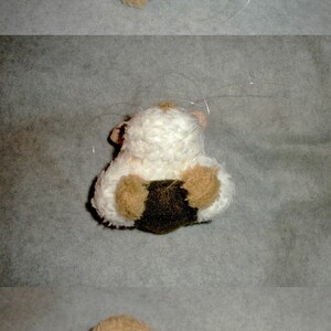 Op de afbeelding: Een bruin en wit pluche hamster speelgoed met lange witte snorharen. Het speelgoed zit op een lichtgrijze ondergrond.