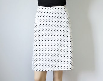 Könnte beinhalten: Weißer Rock mit schwarzem Polka-Dot-Muster. Der Rock ist knielang und hat eine klassische A-Linien-Form. Der Rock wird mit einem schwarzen Oberteil kombiniert.