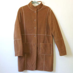 May include: A brown coat with a mandarin collar and button closure. The coat features two front pockets and white stitching details. The coat is hanging on a light green hanger against a white background.