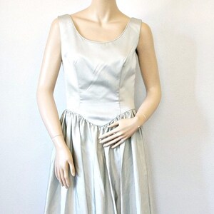 May include: A silver sleeveless gown with a fitted bodice and a full skirt. The gown is made of a shiny satin fabric.