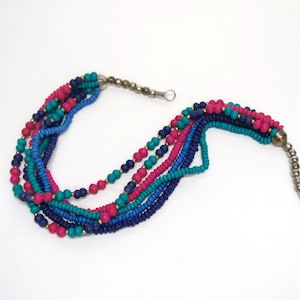 May include: Multi-strand necklace made of small, colorful beads. The necklace is made of turquoise, pink, and blue beads. The necklace has a silver clasp.