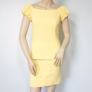 May include: A yellow skirt suit with a fitted skirt and a top with puffed sleeves and a square neckline.