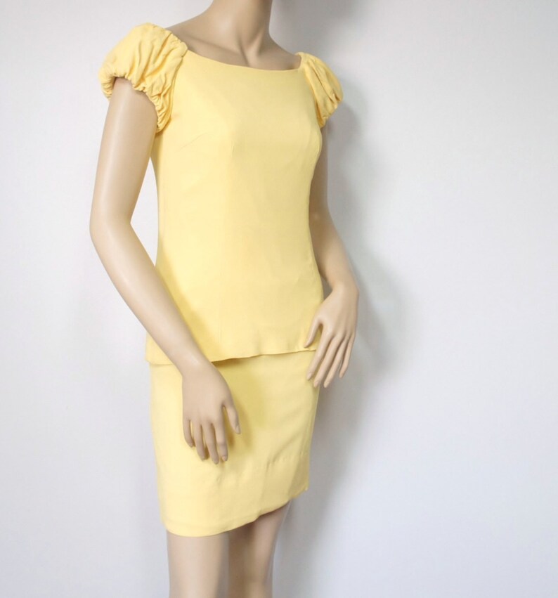 May include: A yellow dress with a fitted bodice and a skirt. The dress has short sleeves with ruched detailing.