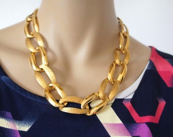 May include: A gold chain necklace with large, textured links. The necklace is thick and chunky, and it is a statement piece.