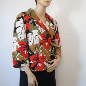 Puede incluir: Una blazer de manga tres cuartos con un estampado floral vibrante. La chaqueta presenta grandes flores de hibisco rojas, hojas blancas y follaje verde sobre un fondo marr&oacute;n y negro. Tiene un cierre de bot&oacute;n negro &uacute;nico y un cuello con muescas.