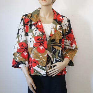 Puede incluir: Blazer con estampado floral con flores de hibisco rojas, hojas verdes y un bot&oacute;n negro. La chaqueta tiene mangas tres cuartos y un fondo blanco. El blazer se muestra en un maniqu&iacute;.