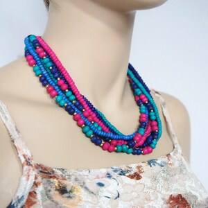 May include: Multi-strand necklace with pink, blue, and turquoise beads. The necklace is layered and has a bohemian style.