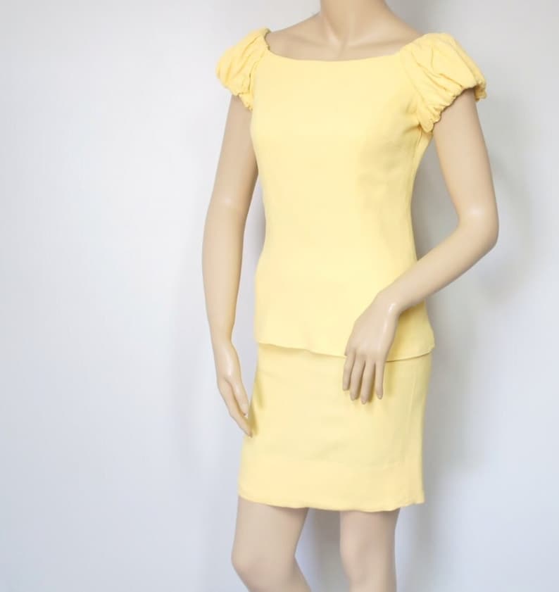 May include: A yellow two-piece outfit with a fitted skirt and a top with puffed sleeves and a boat neck.