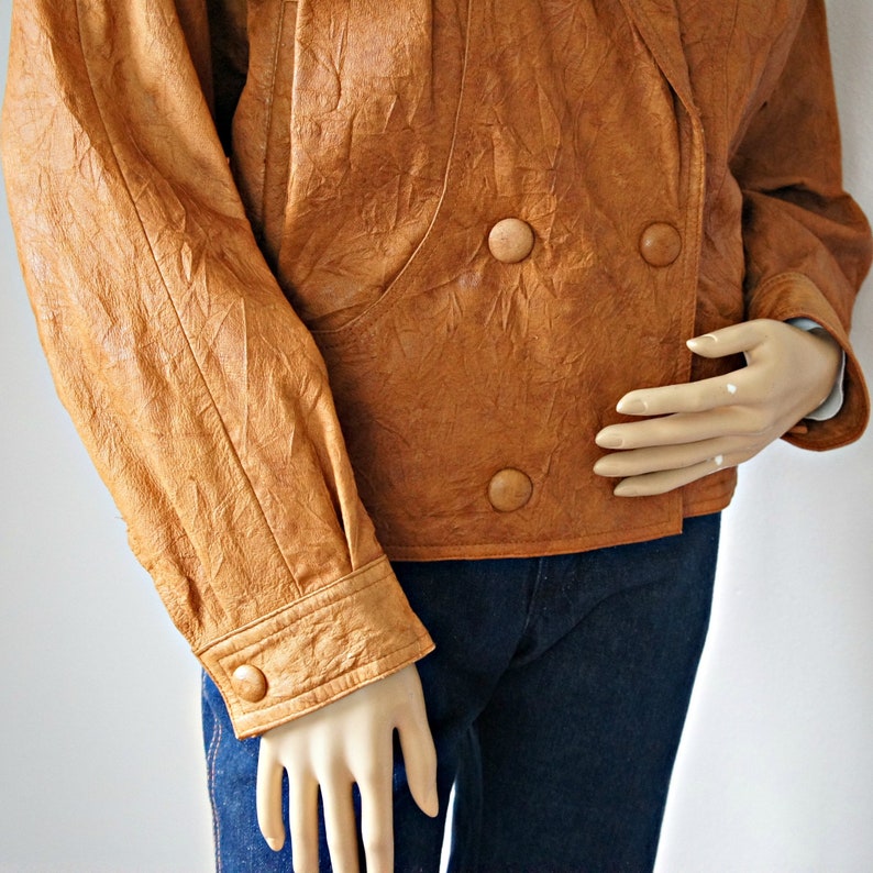 K&ouml;nnte beinhalten: Eine braune Lederjacke mit doppelreihigem Verschluss und vier Kn&ouml;pfen. Die Jacke hat eine strukturierte, geknitterte Optik und ist aus weichem, geschmeidigem Leder gefertigt.