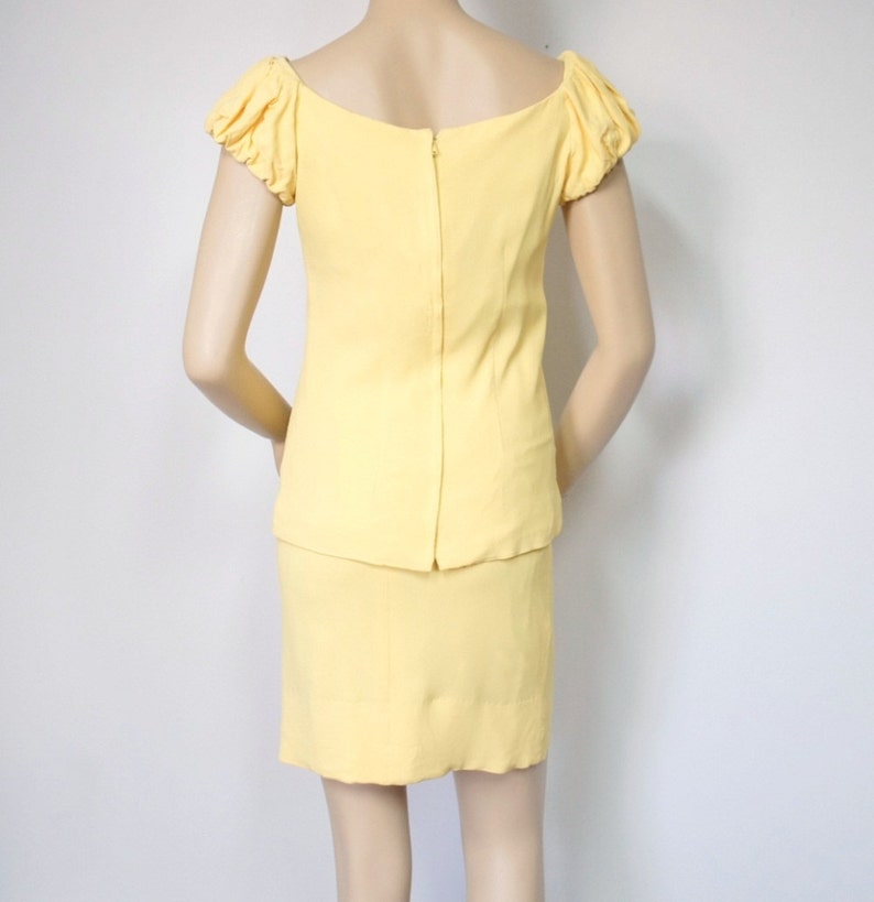 May include: A yellow dress with a fitted skirt and a short-sleeved top with puffed sleeves. The dress has a scoop neckline and a zipper closure in the back.
