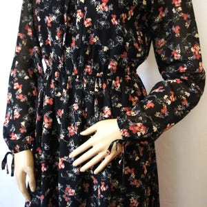 K&ouml;nnte beinhalten: Ein schwarzes, lang&auml;rmliges Kleid mit floralem Muster, einer gerafften Taille und Bindedetails an den &Auml;rmeln.