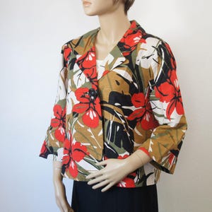 Puede incluir: Una blazer de manga corta con un estampado floral llamativo. La chaqueta presenta grandes flores rojas, hojas verdes y detalles negros sobre un fondo beige y blanco. Tiene un cierre de bot&oacute;n negro &uacute;nico y un dise&ntilde;o de solapa cl&aacute;sico.