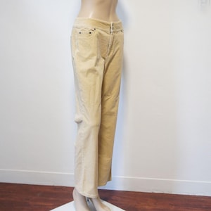 May include: A pair of tan corduroy pants featuring a mid-rise waist, a button and zipper fly closure, and classic five-pocket styling. The trousers have a straight-leg silhouette with visible vertical corded texture throughout the fabric.