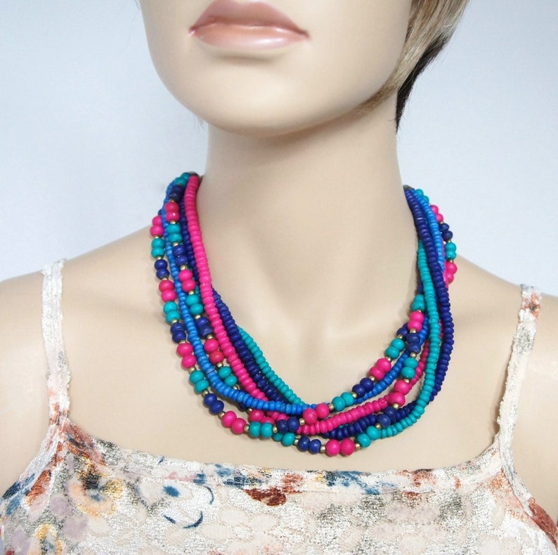 May include: Multi-strand necklace made of colorful beads in shades of teal, blue, and pink. The necklace is layered and has a bohemian style.