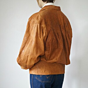 K&ouml;nnte beinhalten: Eine braune Lederjacke mit leicht &uuml;berdimensionierter Passform und einem Knopfschloss vorne.