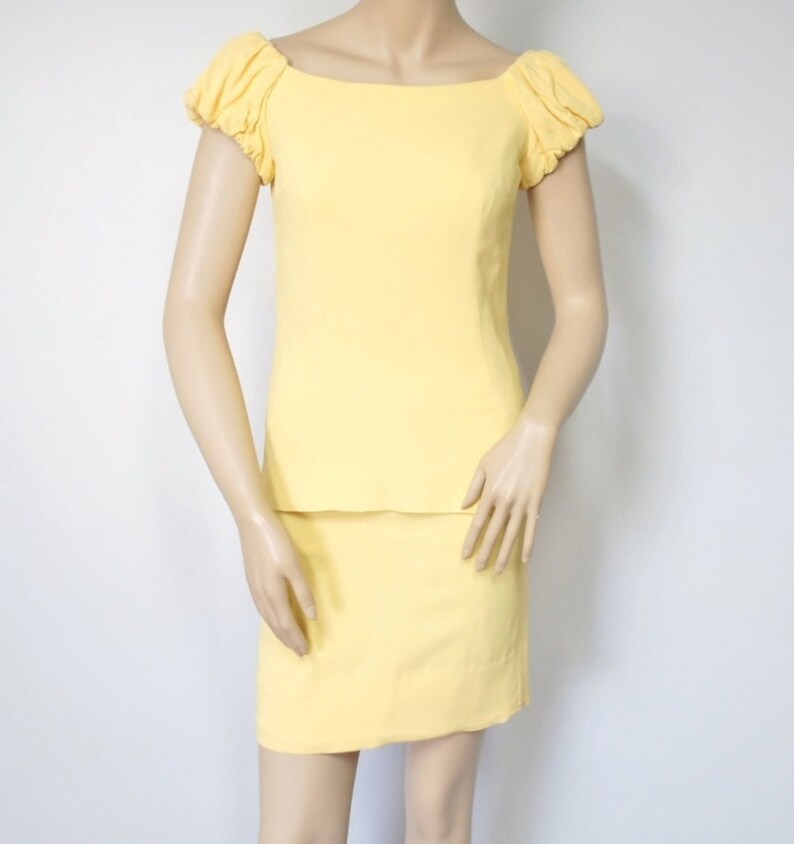May include: A yellow skirt suit with a fitted skirt and a top with puffed sleeves and a square neckline.