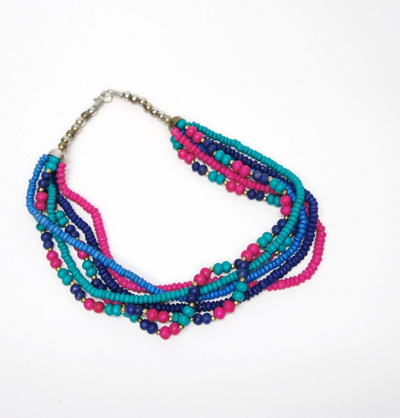 May include: Multi-strand necklace made of small, colorful beads. The necklace features turquoise, pink, and blue beads.