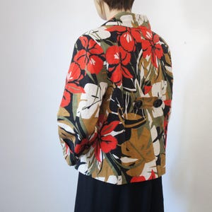 Puede incluir: Chaqueta estampada con un dise&ntilde;o floral en rojo, blanco, negro y marr&oacute;n. La chaqueta tiene mangas largas y dos botones negros en la espalda. El cuello es blanco.