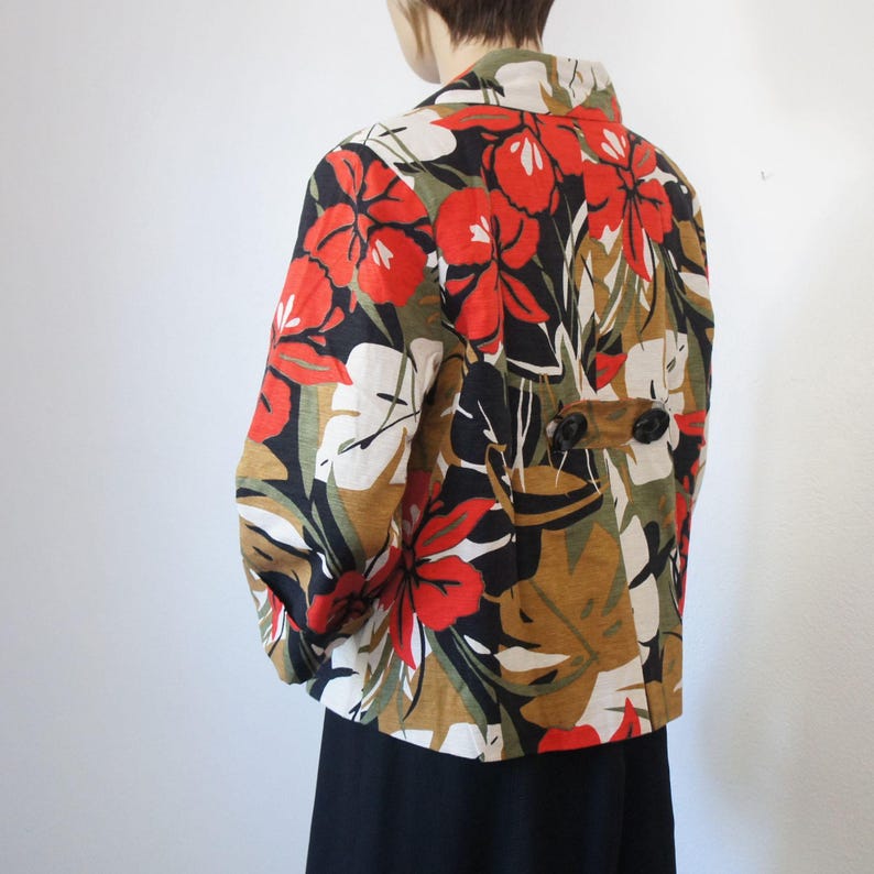 Puede incluir: Chaqueta estampada con un dise&ntilde;o floral en rojo, blanco, negro y marr&oacute;n. La chaqueta tiene mangas largas y dos botones negros en la espalda. El cuello es blanco.