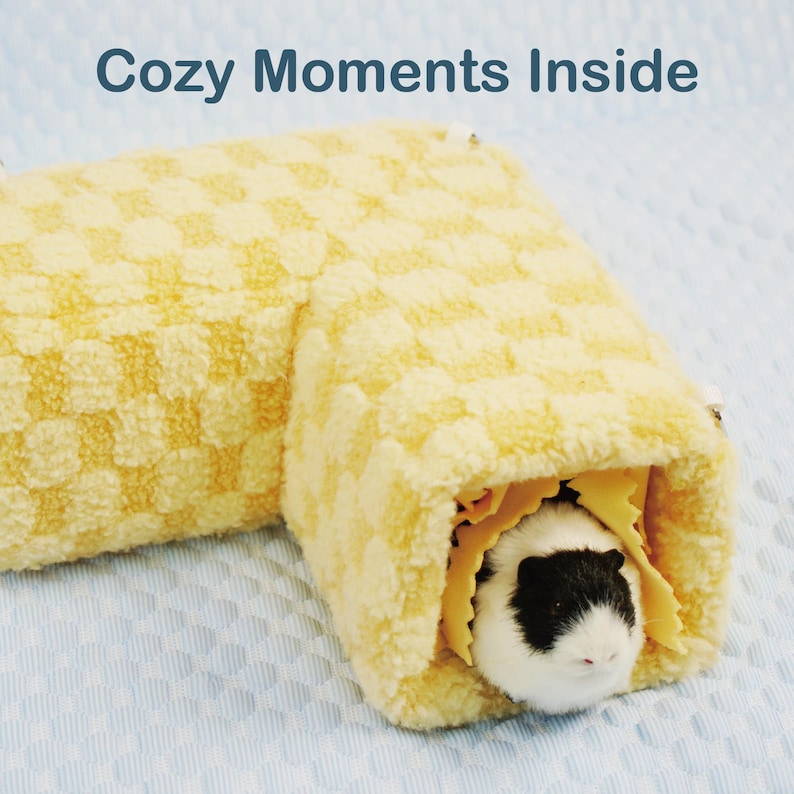 May include: A yellow, checkered pet tunnel with a small guinea pig inside. The guinea pig has black and white fur. The text "Cozy Moments Inside" is at the top of the image. The tunnel is made of a soft, plush material.