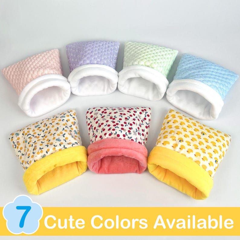 May include: Seven colorful pet bed houses in various patterns and colors, including pink, purple, green, and blue quilted fabrics, and patterned fabrics with yellow, red, and white accents. The beds have a soft, white interior and a yellow or pink trim. The text "7 Cute Colors Available" is at the bottom.
